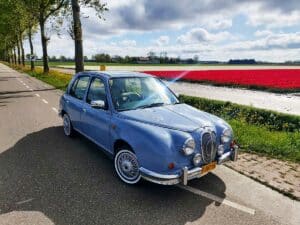Mitsuoka Viewt in pastelblauw, rijdend langs kleurrijke bollenvelden
