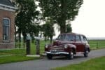 Vooraanzicht van een rijdende Ford Deluxe Fordor Sedan in bordeauxrood